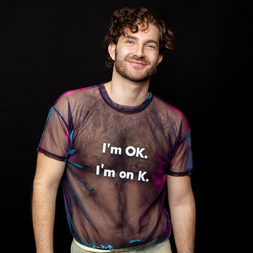 Person wearing a sheer shirt with text 'I'm OK. I'm on K.' against a black background